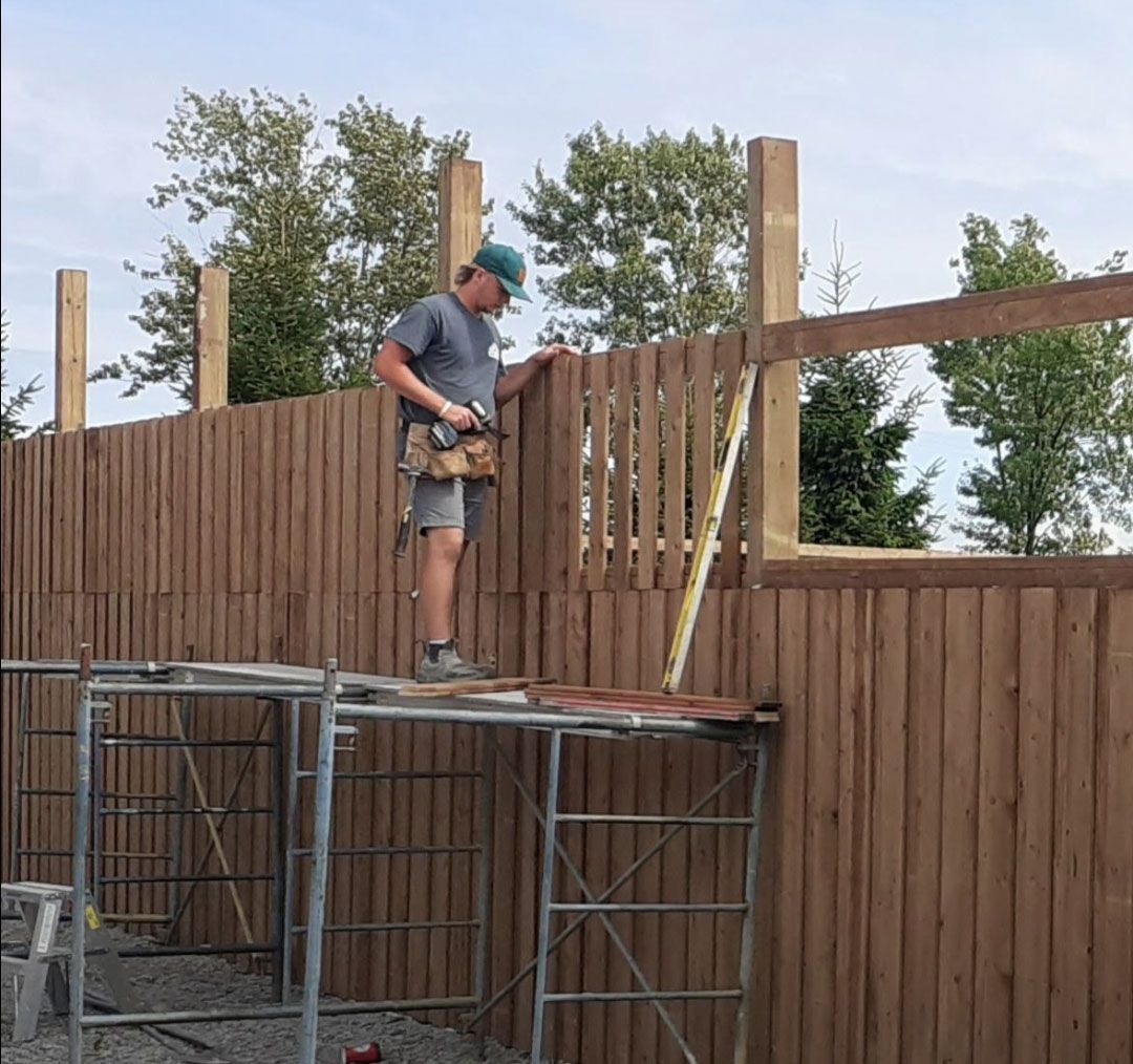 A man is working on a wooden fence on a scaffolding