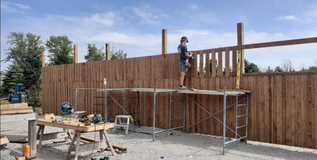 A man is standing on a scaffolding next to a wooden fence.