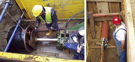 A man wearing a hard hat is working on a machine in a trench.