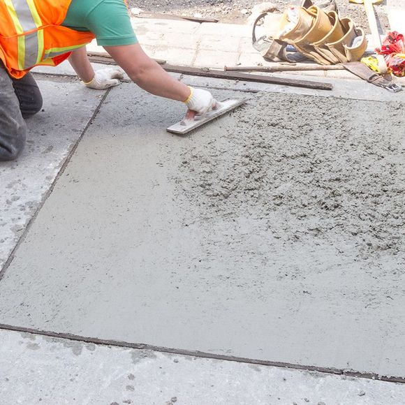 A man is using a trowel to spread concrete on the ground