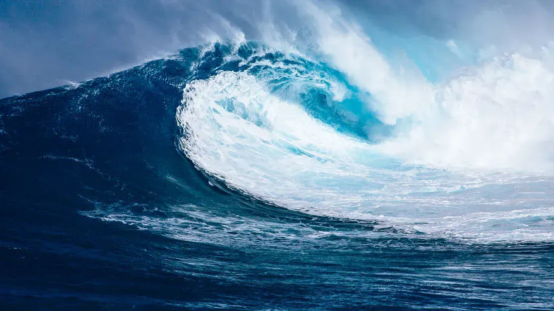 Crashing ocean wave, cresting and breaking with shades of blue and white.