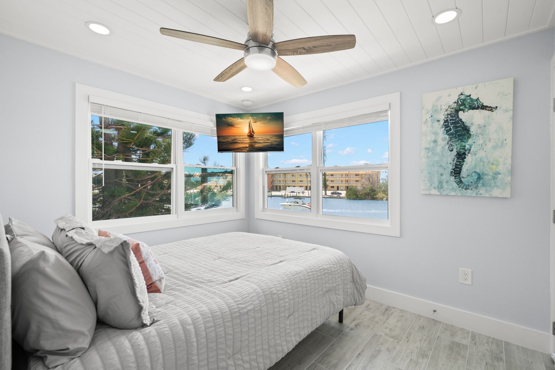 A bedroom with a bed , ceiling fan , television and a painting of a seahorse on the wall.