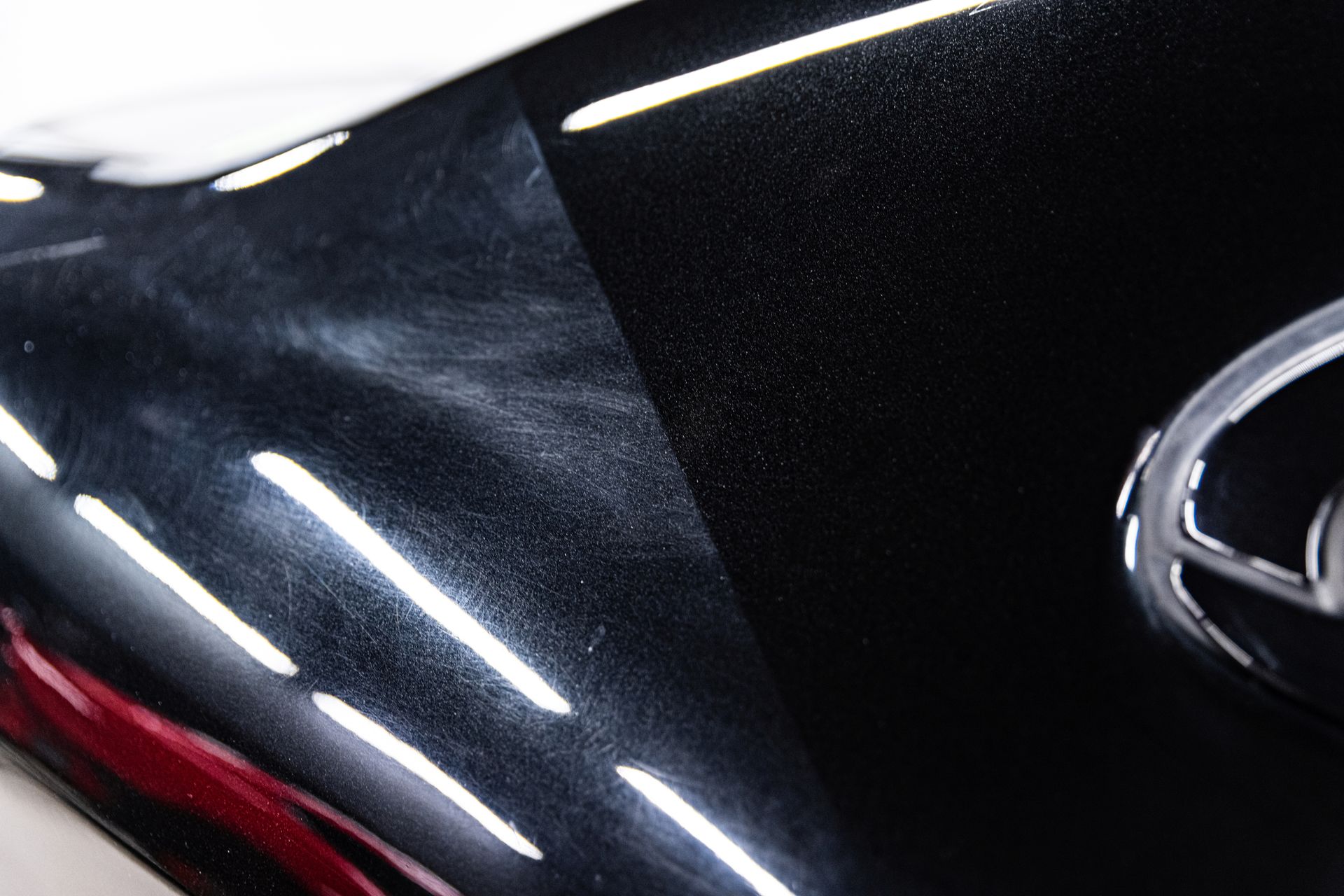 A black car surface featuring a swirl-marked section next to a polished area, showing a clear contrast in paint condition.
