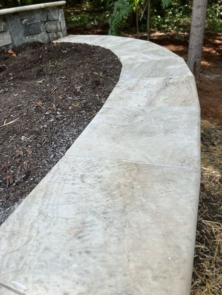 Curved light stone walkway beside a mulched garden bed and trees