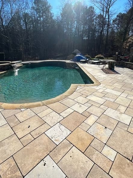 Backyard pool with turquoise water and tan stone patio in bright sunlight