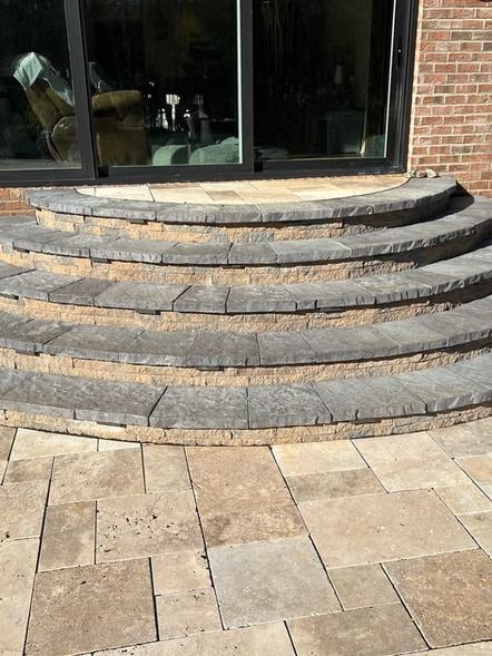 Curved stone steps leading to a glass storefront entrance with tan paver patio foreground