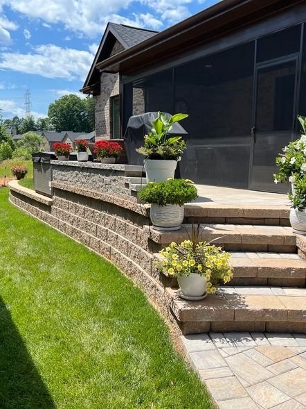 Modern house front with stone steps, potted flowers, and a manicured green lawn