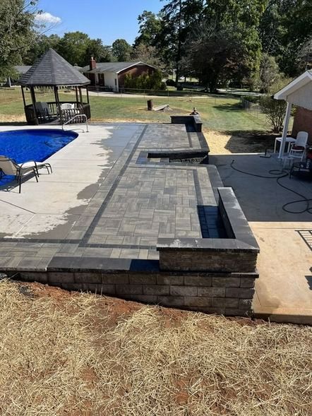 Backyard patio with gray pavers, built-in fire pit, pool, gazebo, and surrounding lawn on a sunny day