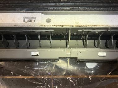 Close-up of an exposed mechanical interior with wires, vents, and metal panels under a dim surface.