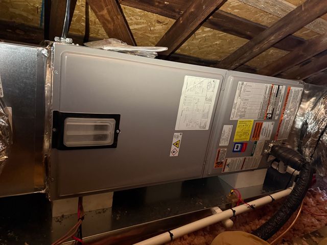 Furnace and ductwork in an attic, with silver insulated HVAC unit and exposed wooden rafters.