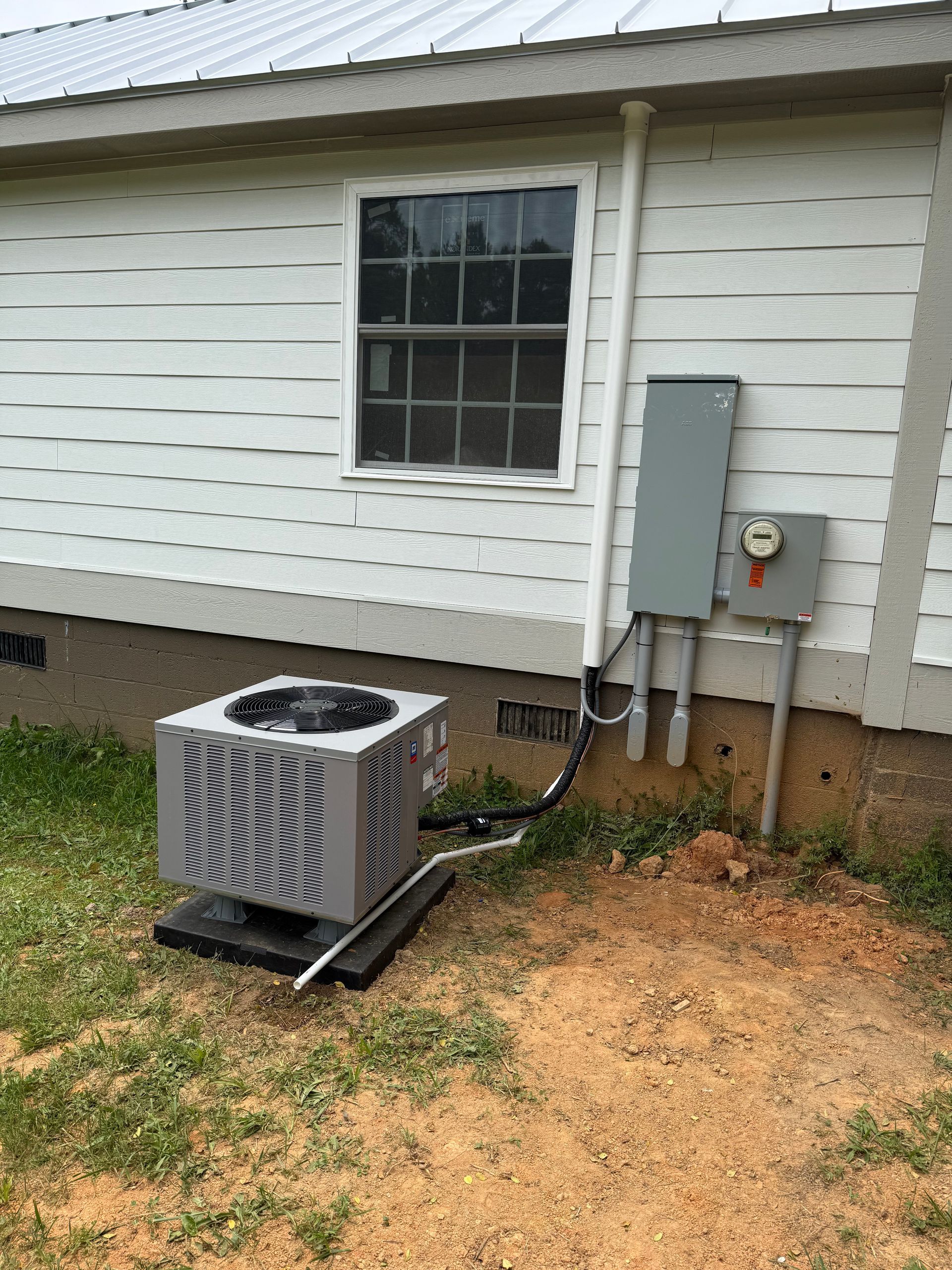 Outdoor air conditioner unit beside a white house wall with a window and electrical panel