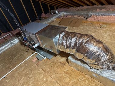 Attic HVAC ductwork with insulated metal vent and flexible foil duct on plywood floor