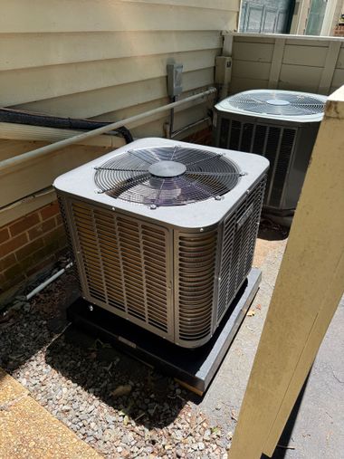 Two outdoor air conditioning units beside a house, with frost or snow on the front unit.