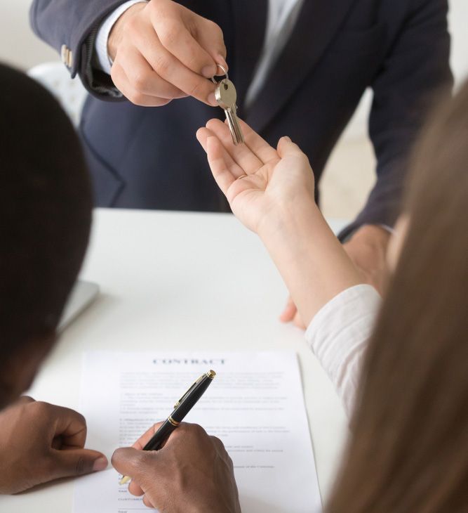 A Man is Giving a Key to a Woman Who is Signing a Contract — Budd & Piper Solicitors & Conveyancers in Tweed Heads, NSW