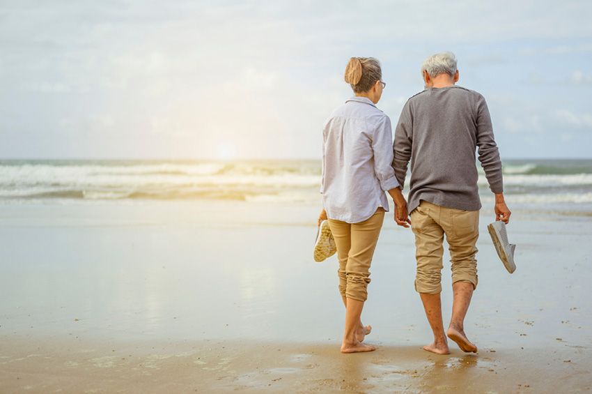 An Elderly Couple is Walking on the Beach Holding Hands — Budd & Piper Solicitors & Conveyancers in Tweed Heads, NSW