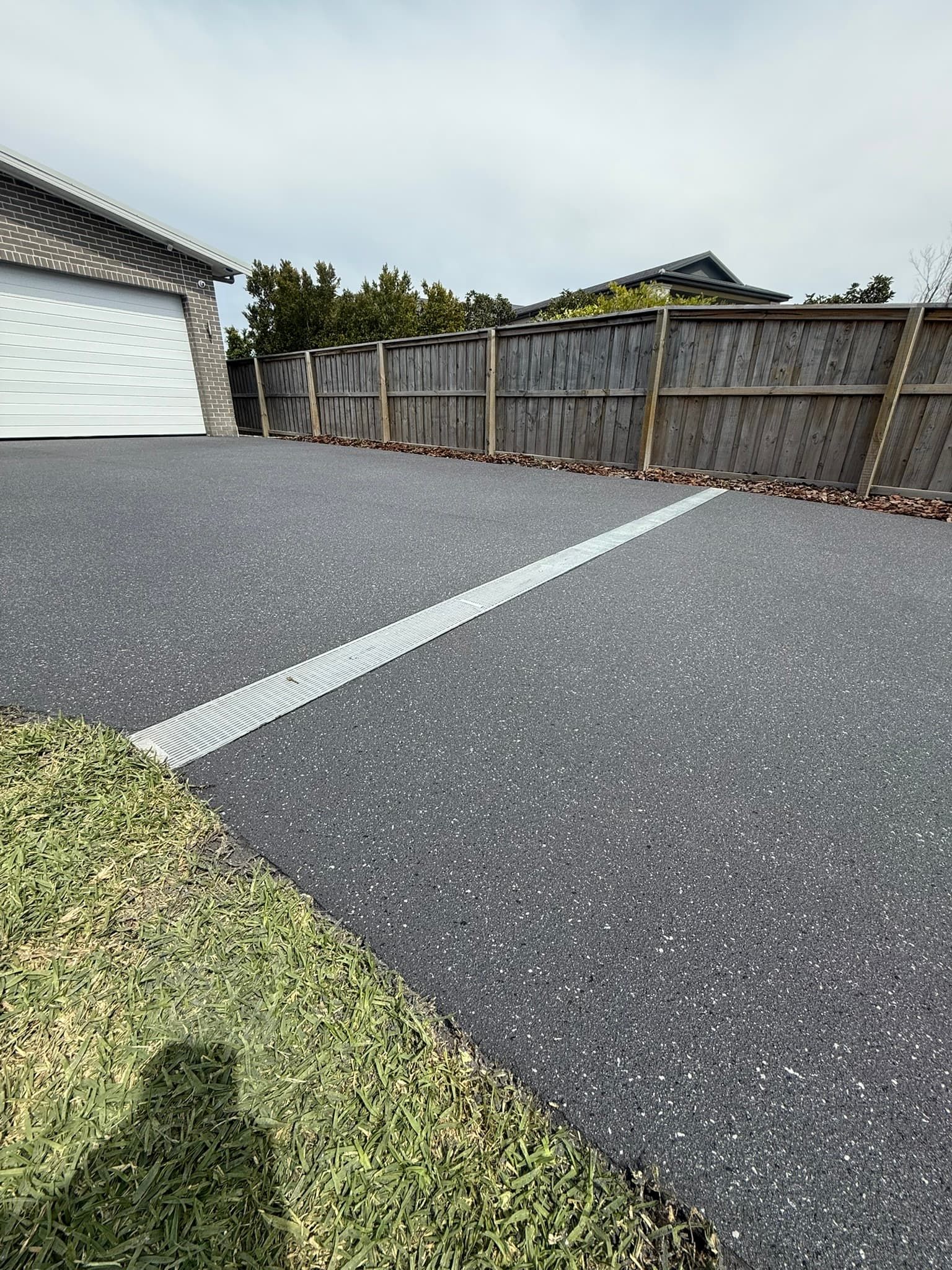 Gray Driveway with A Drain, Next to Grass and Fence — Port Macquarie Concrete Resurfacing in Port Macquarie, NSW