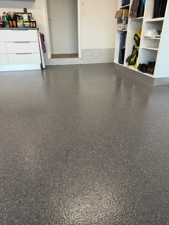 Grey epoxy-coated garage floor with cabinets, door, and shelves filled with items — Port Macquarie Concrete Resurfacing in Port Macquarie, NSW