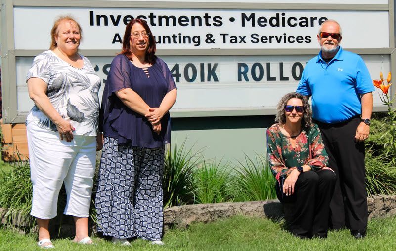 Four people standing in front of a business sign. Light-skinned people, 3 women, 1 man. Blue, white, and floral clothing.