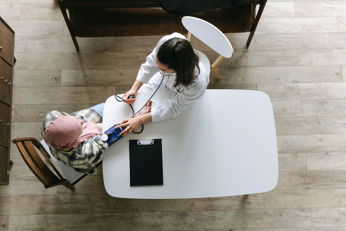 Doctor taking patient's blood pressure at a white table in a medical setting.