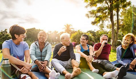 Group of people sitting outdoors on a sunny day, smiling and laughing.