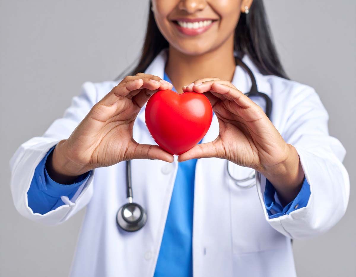 Doctor holding a red heart, smiling, wearing a stethoscope and lab coat.