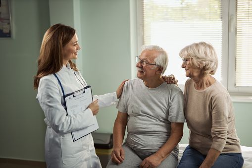 Doctor speaking with an elderly couple in a medical office; doctor has arm around man.