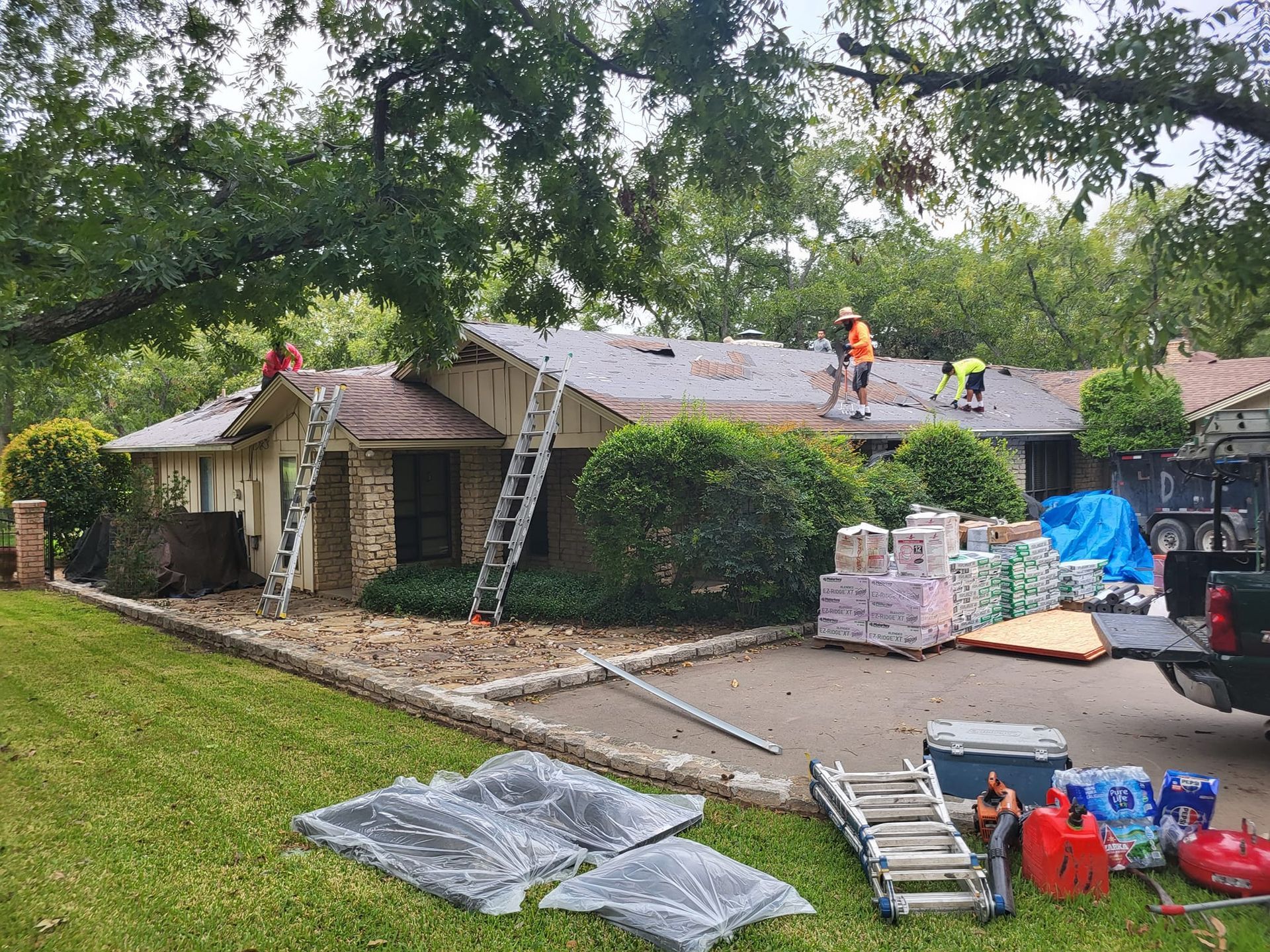 Roofers replacing shingles on a house, materials, and equipment on the ground and truck.
