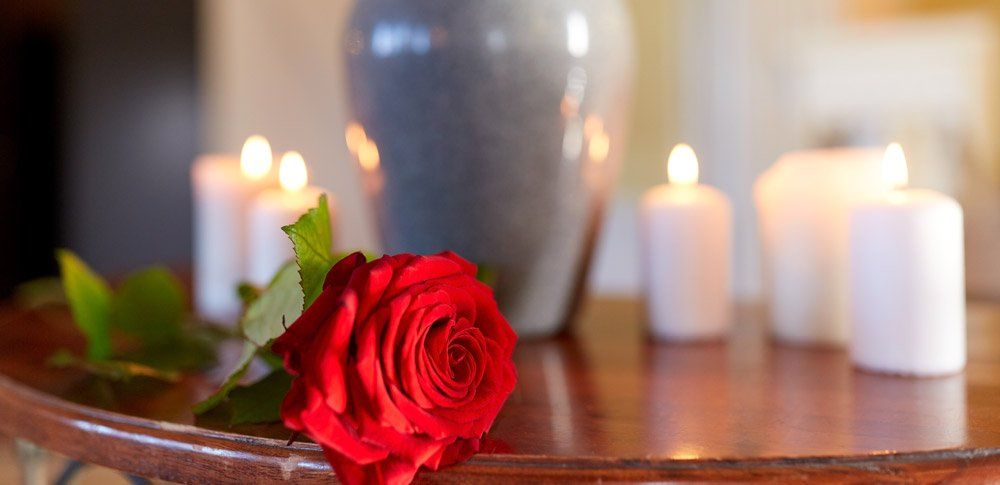 Red rose and cremation urn with burning candles