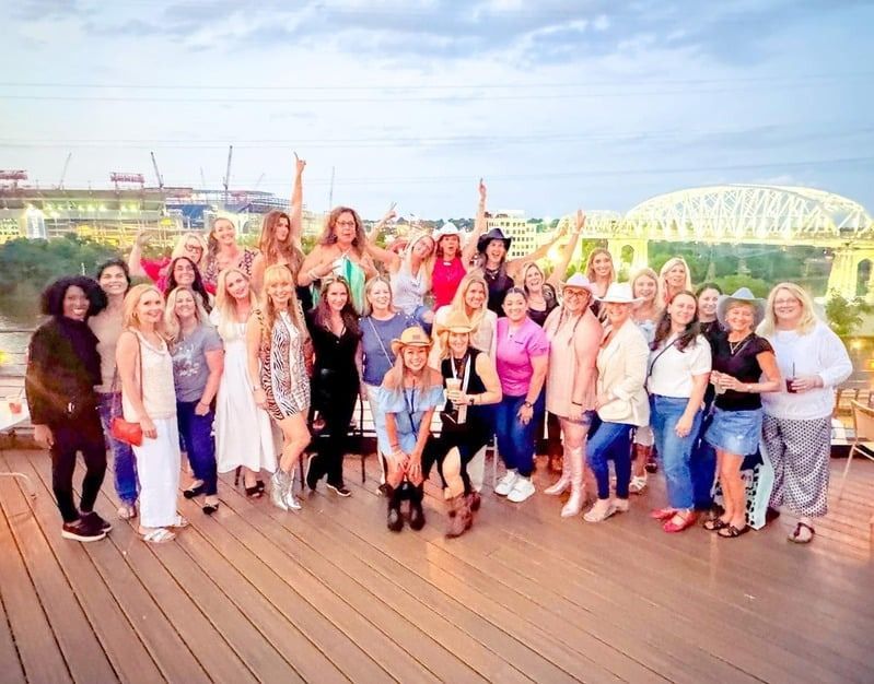 Group of people posing on a wooden deck at sunset with a bridge in the background.