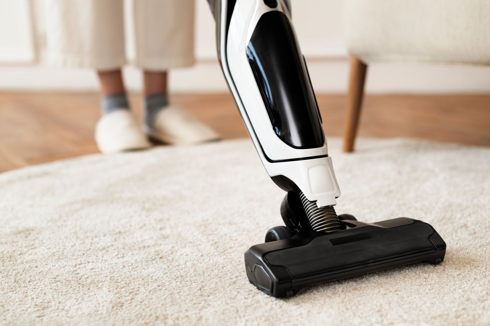 Person vacuuming a white rug with a black and white vacuum cleaner.
