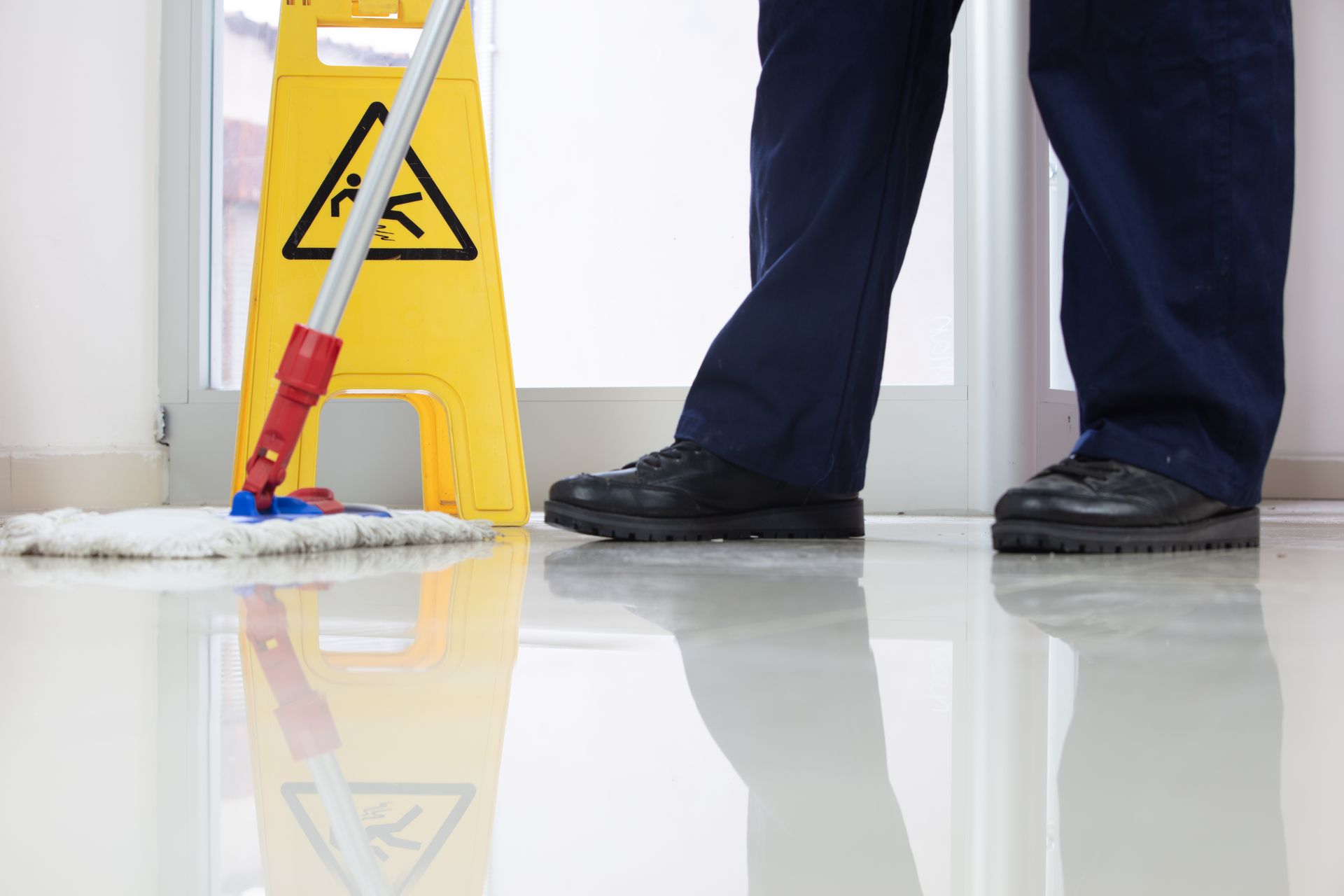 A person mopping a shiny floor with a caution sign.