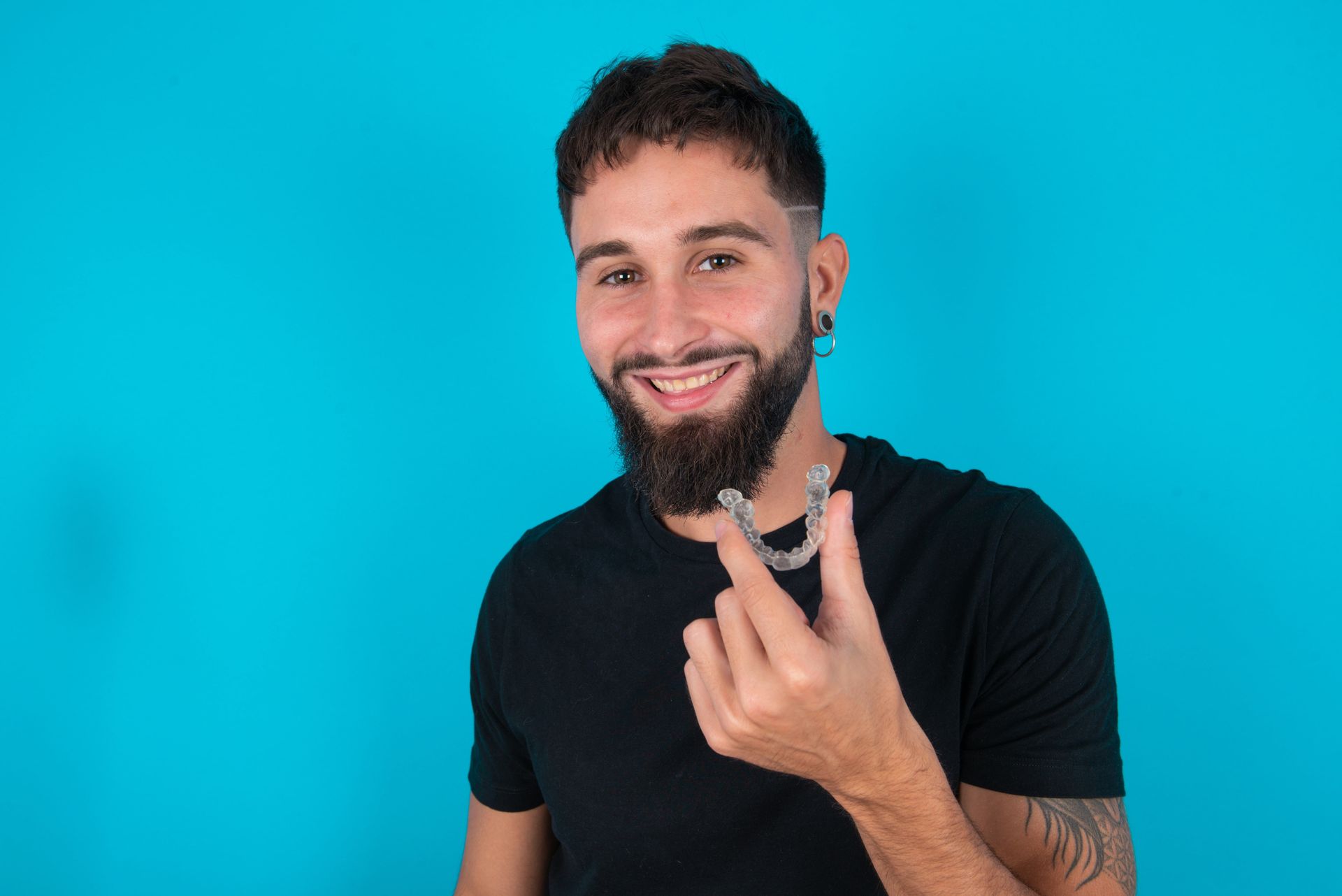 A man with a beard is holding a mouth guard in his hand.