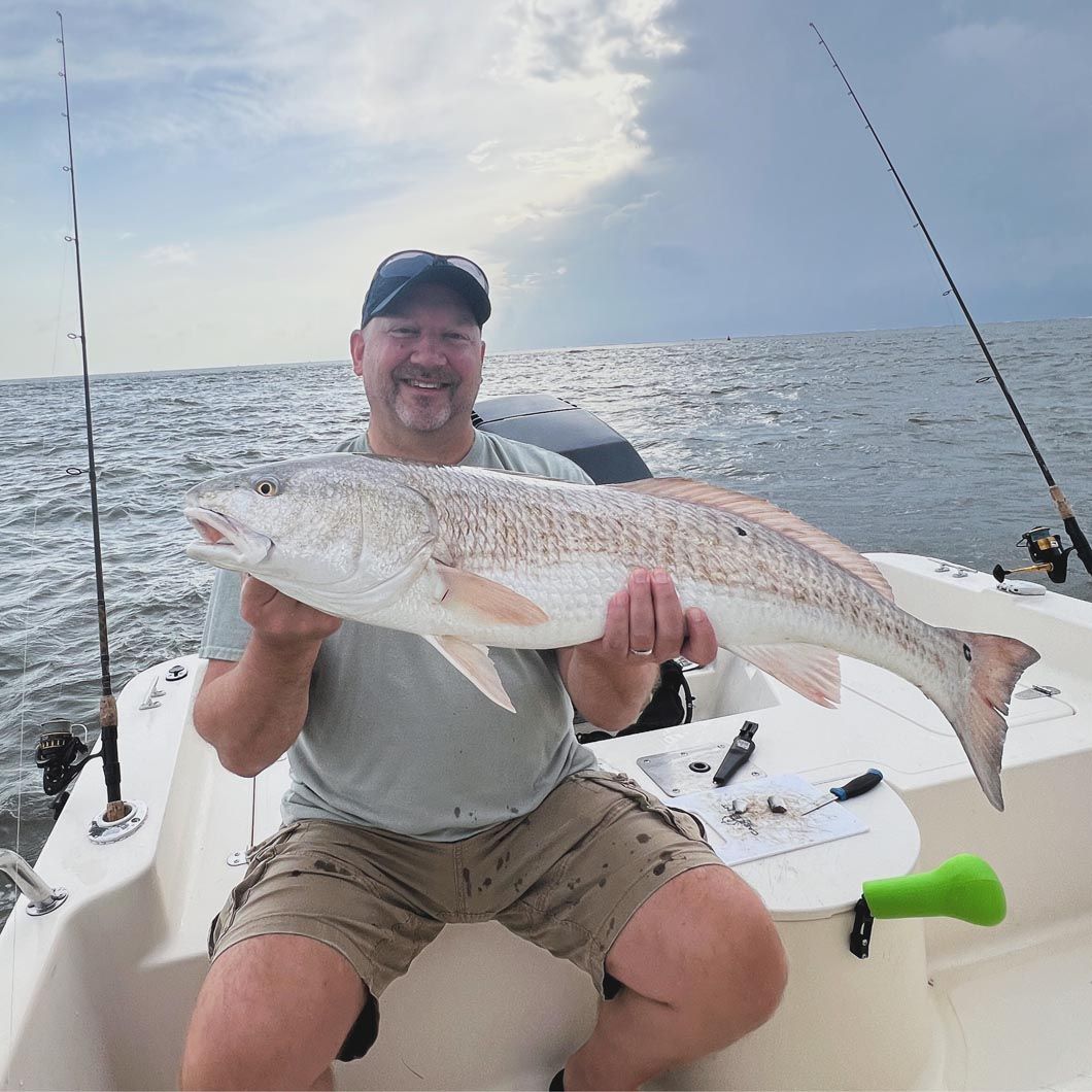 A man is sitting on a boat holding a large fish in his hands.