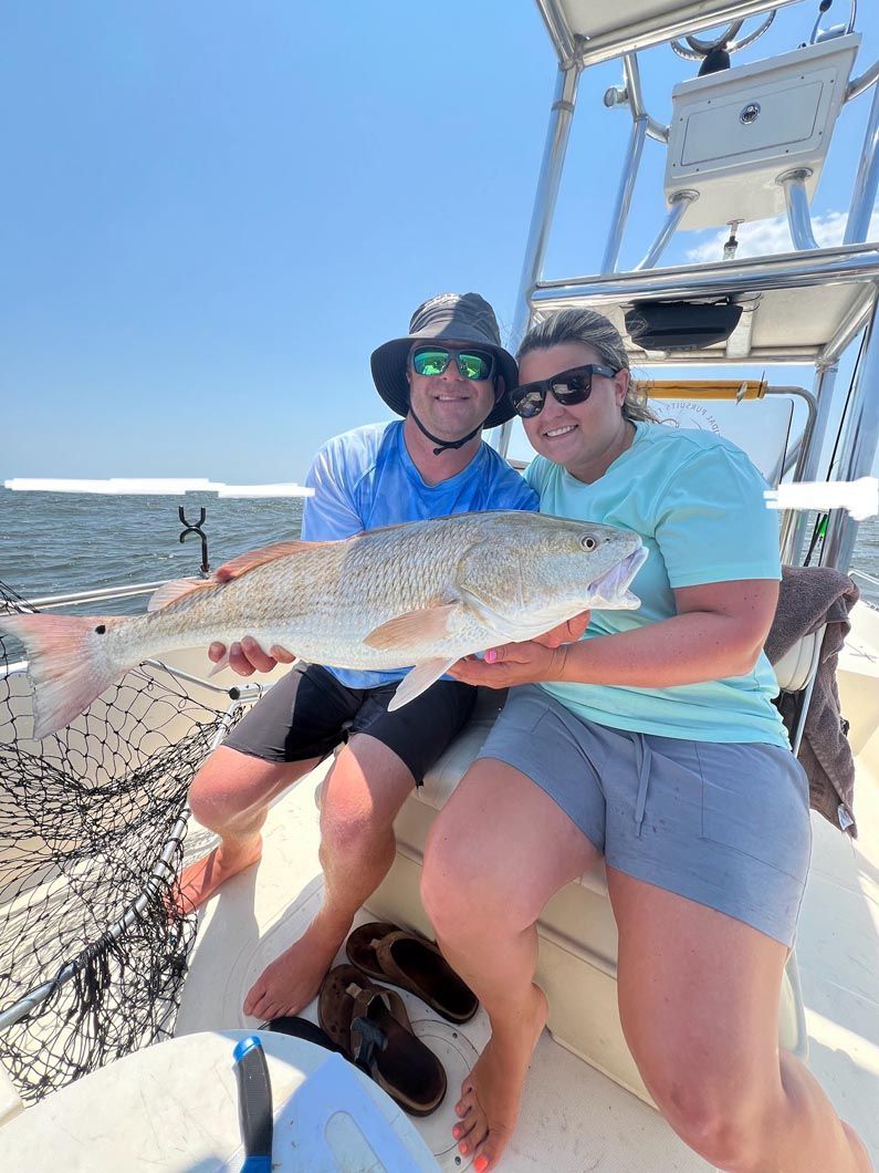 A man and a woman are sitting on a boat holding a large fish.
