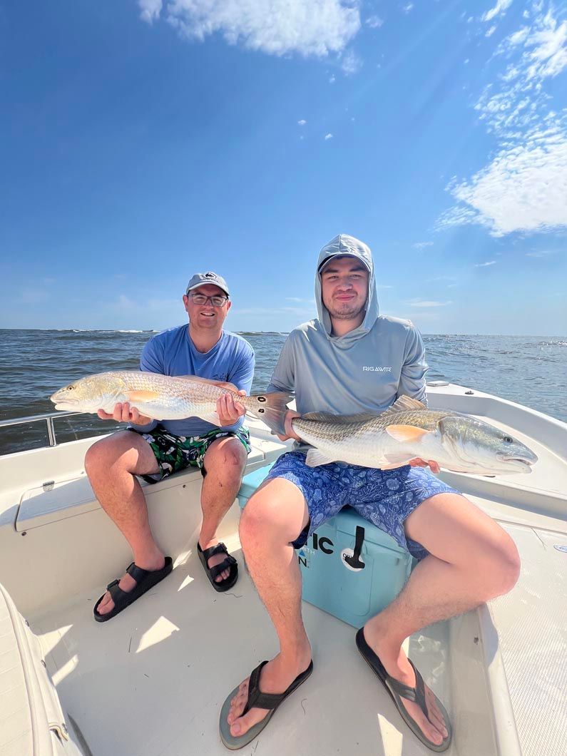 Two men are sitting on a boat holding fish.