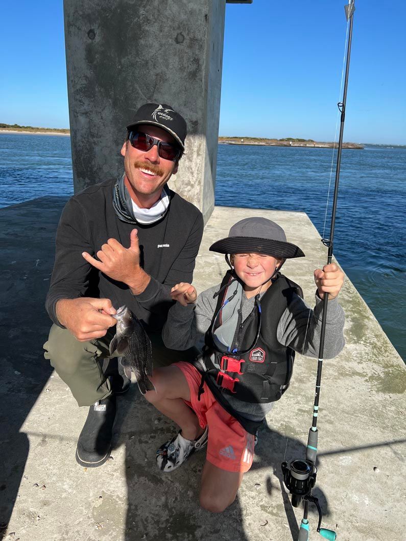 A man and a boy are sitting on a pier holding fishing rods.