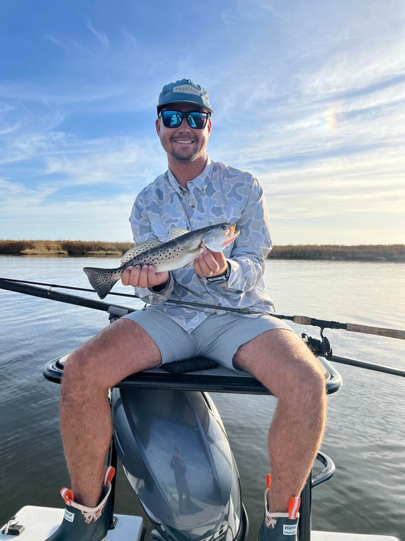 A man is sitting on the back of a boat holding a fish.