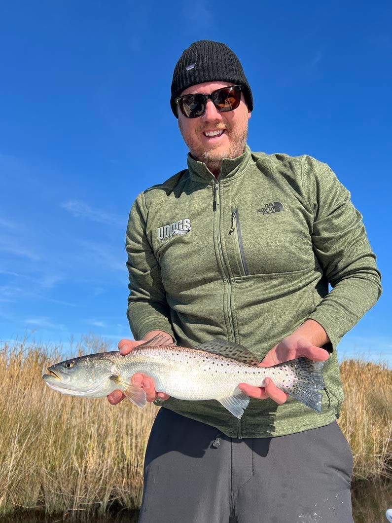 A man in a green jacket is holding a fish in his hands.