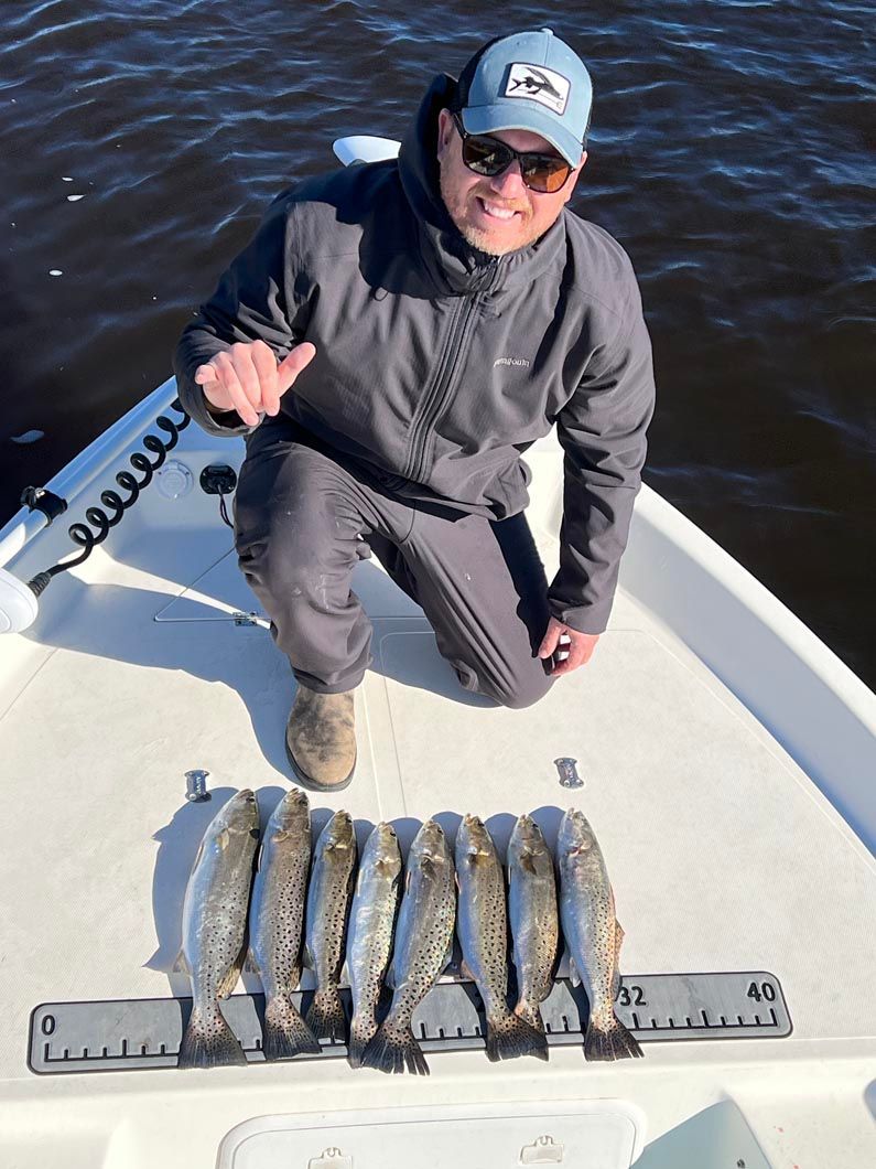 A man is kneeling on the deck of a boat holding a bunch of fish.
