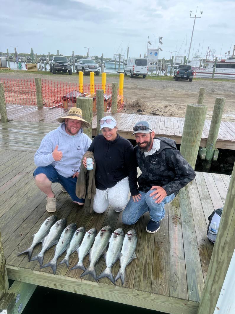 Three men are kneeling on a dock holding fish.