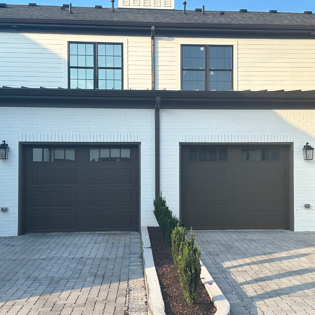 A white house with two garage doors and a brick driveway
