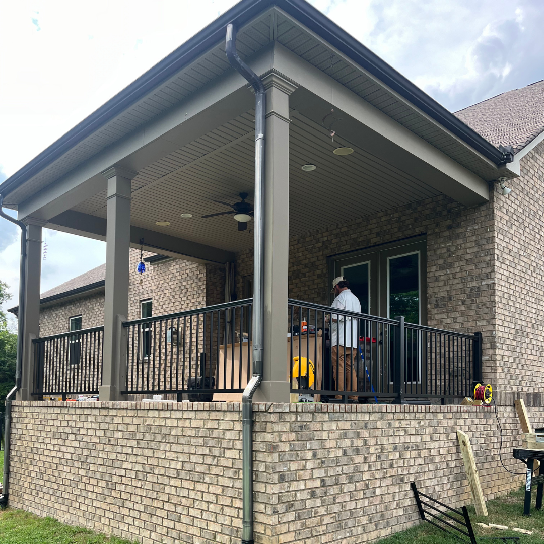 A man is standing on a porch of a brick house.
