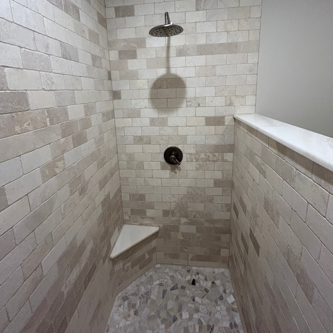 There is a shower with a brick wall and a tiled floor.