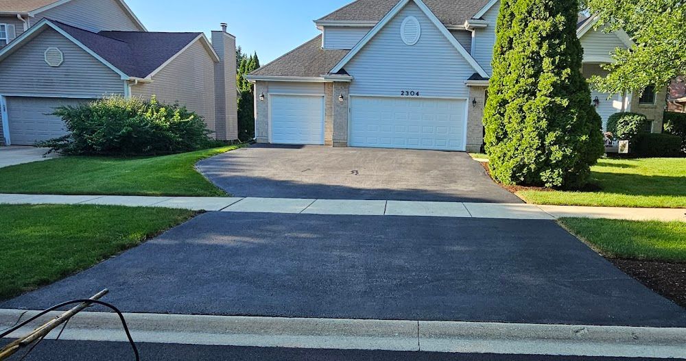 Residential driveway resurfaced with dark asphalt in front of two beige suburban garage doors