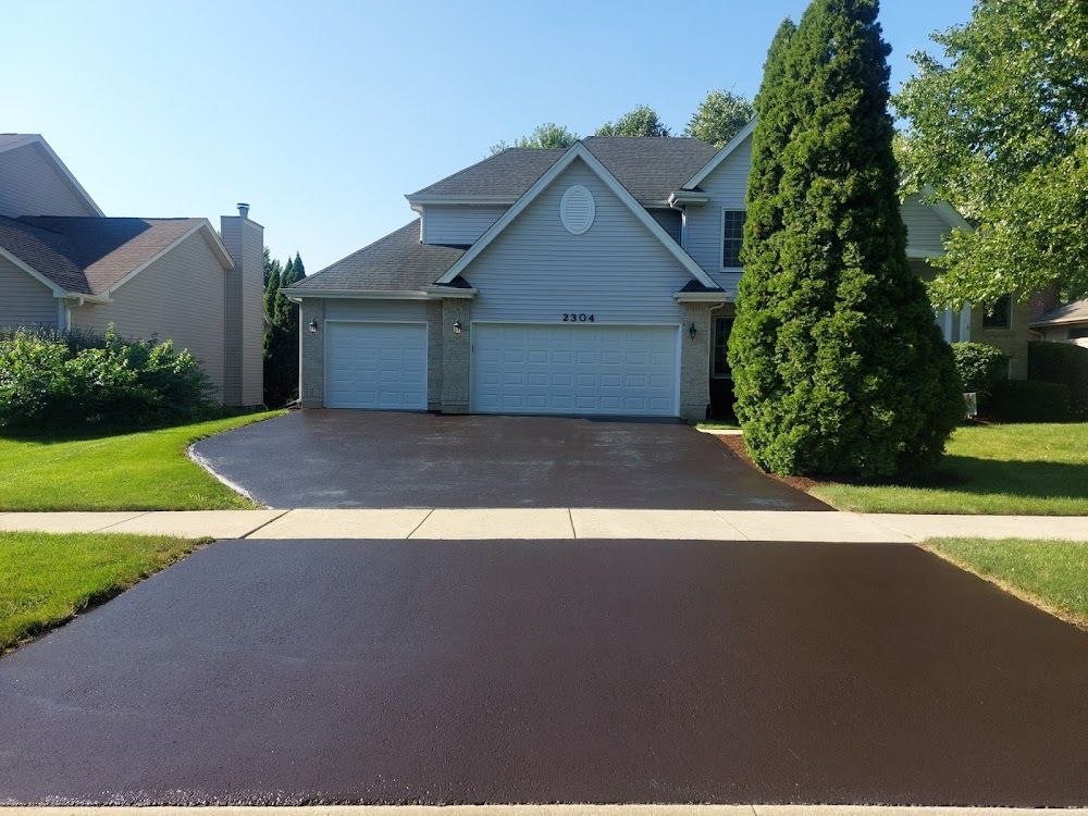 Suburban house with a two-car garage and a freshly paved dark driveway on a sunny day