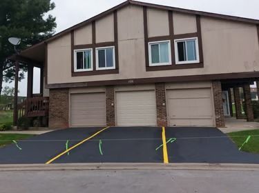 Two-story brown building with three garage doors and a paved parking lot in front