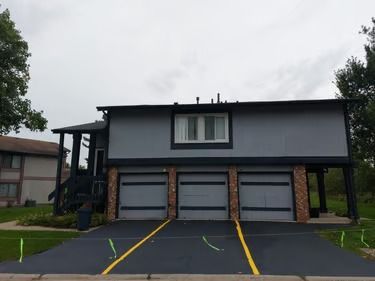 Three-story gray apartment building with four garage doors and yellow parking lines in front