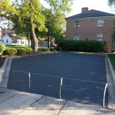 Black tarp covering a sloped driveway beside a brick house and trees.