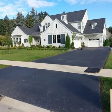 White suburban house with black roof and driveway, front lawn, and garage under a clear sky