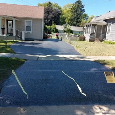 Freshly paved dark driveway between two houses, leading to a small fenced backyard.